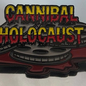 May include: A pin badge with the words "CANNIBAL HOLOCAUST" in yellow and red dripping letters. The badge is shaped like film reels and has a dark grey and red colour scheme. It is likely a collectible item.