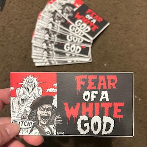 May include: Rectangular stickers with the text "FEAR OF A WHITE GOD" in red dripping font on a black background. The left side features a cartoon illustration of a figure pointing and another figure wearing a beret. The word "BITCH!" is also present.