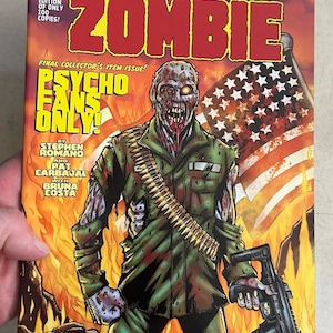 May include: Comic book cover featuring a zombie soldier with a bloody face and a gun. The cover is red, white, and blue with flames in the background. The title is "Lucio Fulci's Zombie" and the tagline is "Psycho Fans Only!"