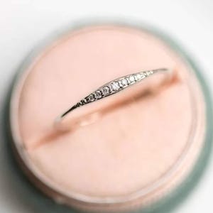 May include: A delicate silver ring with a row of small, clear gemstones set in a curved band.