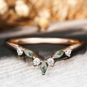 Könnte beinhalten: Ein zarter Roségold-Ehering mit einem geschwungenen Design, das mit einer Reihe von marquiseförmigen grünen und weißen Edelsteinen besetzt ist.