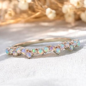 May include: A delicate gold band ring with a row of small, iridescent opal gemstones set in a chevron pattern.