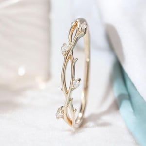 Puede incluir: Un delicado anillo de oro con un diseño de vid y pequeñas piedras transparentes. El anillo es una pieza de joyería simple y elegante.