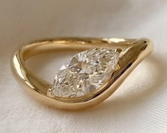 May include: A gold ring with a unique, flowing design. The ring features two marquise-cut diamonds set side-by-side, creating a sparkling focal point. The band is smooth and polished, with a subtle curve that adds to its elegant appeal.