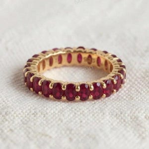 Peut inclure: Une bague alliance en or jaune, ornée d'une rangée continue de pierres précieuses rouges taille ovale, fixées par des griffes partagées. La bague présente une finition métallique polie et une disposition uniforme des pierres sur tout l'anneau.
