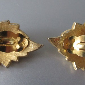 May include: A pair of gold-tone clip-on earrings with a leaf design. The back of the earrings are marked "JONAV".