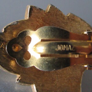 May include: Gold-toned clip-on earrings with a leaf-shaped design. The back of the earrings are marked "JOMAZ."
