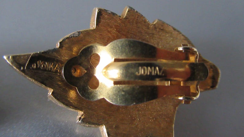 May include: Gold-toned clip-on earrings with a leaf-shaped design. The back of the earrings are marked "JOMAZ."