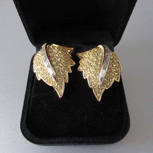 May include: A pair of gold tone leaf-shaped earrings with clear and yellow rhinestones. The earrings are in a black velvet jewelry box.
