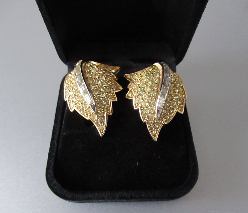 May include: A pair of gold tone leaf-shaped earrings with clear and yellow rhinestones. The earrings are in a black velvet jewelry box.