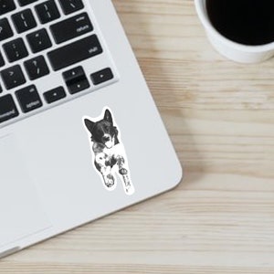 May include: Black and white sticker of a dog with its tongue sticking out. The dog is lying on its side with its head turned to the side.