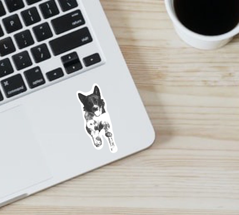 May include: Black and white sticker of a dog with its tongue sticking out. The dog is lying on its side with its head turned to the side.