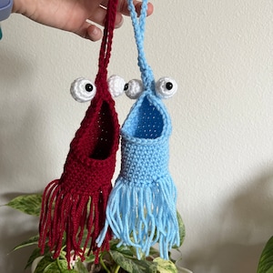 May include: Two crocheted hanging ornaments with googly eyes and fringe. One is red and the other is blue.