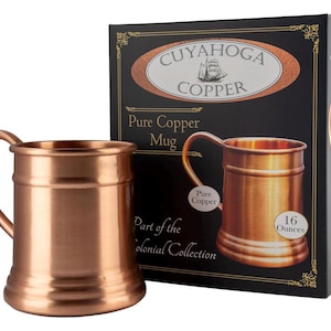 Op de afbeelding: Een koperen mok met een handvat, naast de productdoos. De mok is gemarkeerd met "Pure Copper" en bevat ongeveer 473 ml. De doos toont het "Cuyahoga Copper"-logo en de woorden "Part of the Colonial Collection."