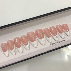 May include: A set of ten false nails with a white french tip design and pearl accents. The nails are in a box with the text "@angeltips.co" on the bottom.