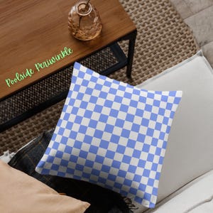 May include: A square throw pillow with a blue and white checkerboard pattern. The pillow is on a white couch. The words "Poolside Periwinkle" are in green script in the upper left corner.