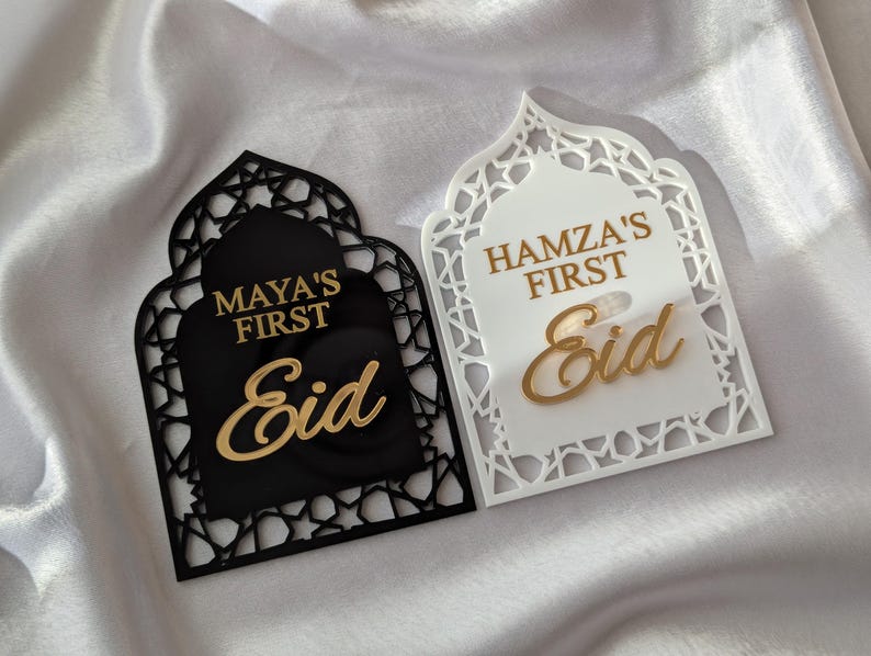 Peut inclure: Deux plaques d&eacute;coratives pour l'A&iuml;d. L'une est noire avec le texte dor&eacute; "Maya's First Eid". L'autre est blanche avec le texte dor&eacute; "Hamza's First Eid". Les deux plaques ont une forme arqu&eacute;e avec des motifs d&eacute;coup&eacute;s.