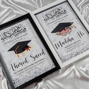 May include: Two framed graduation announcements. One has a black frame, the other a white frame. Both feature calligraphy, a graduation cap, and the names "Ahmed Saeed" and "Madiha Ali" with graduation details. Clear crystals line the bottom.