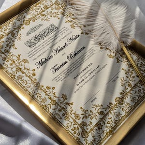 May include: A framed wedding certificate with gold floral detailing and calligraphy. The document features the names Muhsin Haseeb Nasir and Tasnim Rehman, and the date September 10, 2015. A white feather quill rests on the frame.