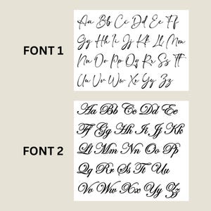 May include: Two handwriting font samples are shown. The first, labelled "FONT 1", displays a cursive alphabet in black ink. The second, labelled "FONT 2", also presents a cursive alphabet in black ink. Both fonts are set against a light beige background.