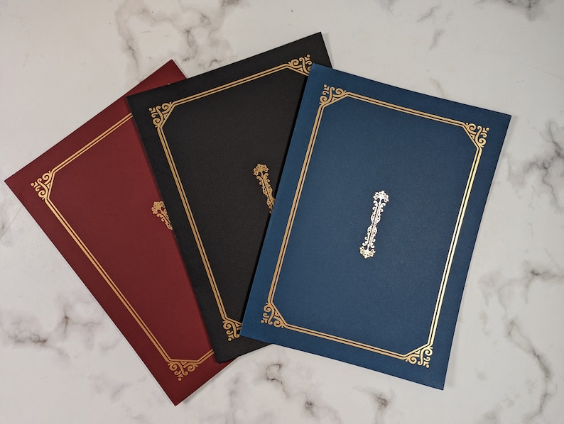 May include: Three document holders in burgundy, black, and navy blue, each with a gold border and decorative corner accents. A gold emblem is centered on each holder, creating a classic and elegant design.