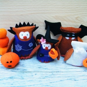 Op de afbeelding: Vier Halloween-kostuums van vilt in de vorm van een uil met oranje pompoenen. De uilen dragen heksenhoeden, een vleermuiskostuum en een spookkostuum.