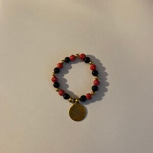 May include: A red and black beaded bracelet with a gold charm that says "Every journey begins with one step".