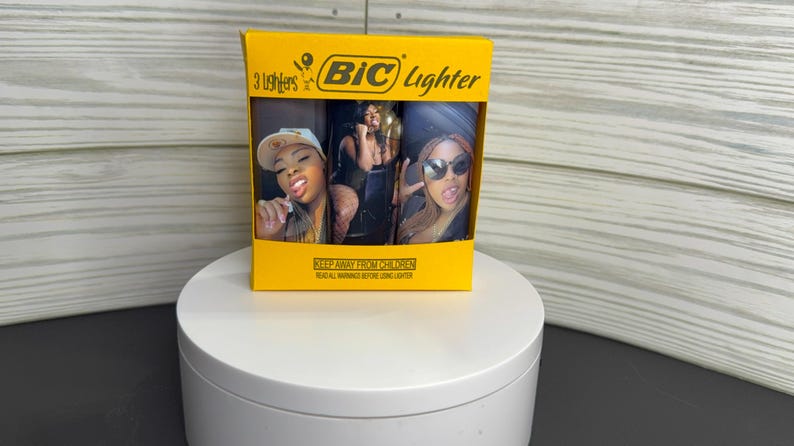 May include: A yellow BIC lighter package containing three lighters. Each lighter features a different image of a woman. The package has the BIC logo and the text "3 Lighters". The bottom of the package has the text "KEEP AWAY FROM CHILDREN".