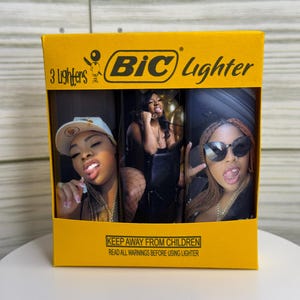 May include: A yellow box containing three BIC lighters. Each lighter features a different image of a person. The box has the BIC logo and text that reads "3 Lighters" and "KEEP AWAY FROM CHILDREN".