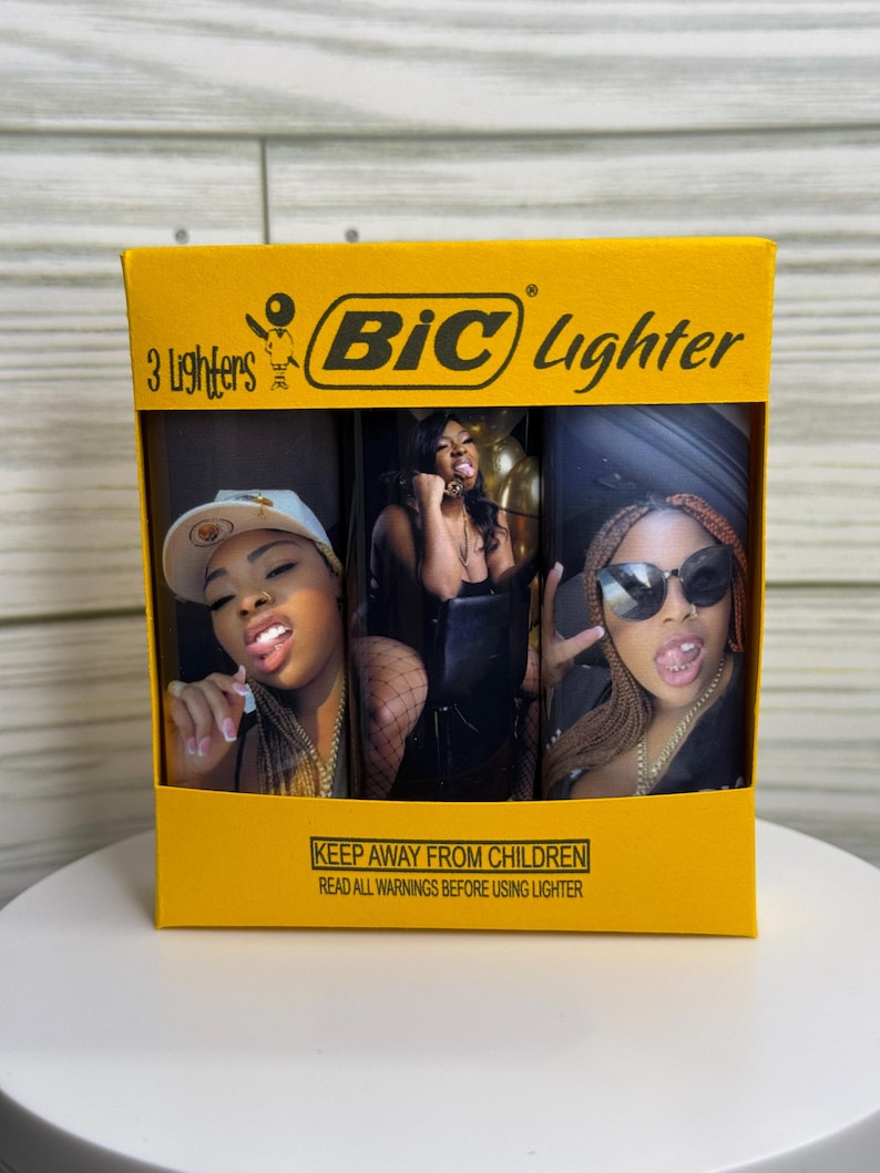 May include: A yellow box containing three BIC lighters. Each lighter features a different image of a person. The box has the BIC logo and text that reads "3 Lighters" and "KEEP AWAY FROM CHILDREN".