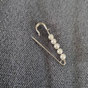 safety pin in silver metal with white pearl attaches wedding dress train, waistcoat or jacket clasp