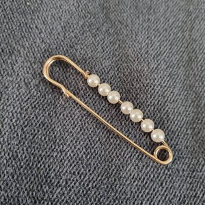 gold metal safety pin with white pearl attaches wedding dress train, waistcoat or jacket clasp