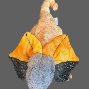 May include: A plush toy shaped like a frilled lizard with orange and yellow scales and a gray head. The lizard has black and orange frills around its head.