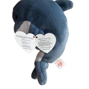 May include: A blue and white plush dolphin Beanie Baby toy with a red heart-shaped tag that reads "Waves style 4084 DATE OF BIRTH: 12-8-96 Join him today on the internet Don't be afraid to get your feet wet He taught all the Beanies how to surf Our web page is his home turf Visit our web page!!! http://www.ty.com"