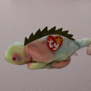 May include: A tie-dye green, pink, and blue chameleon Beanie Baby with a green felt spiky back and a red Ty tag with a white star.
