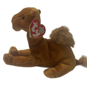 May include: A brown camel Beanie Baby plush toy with a red Beanie Baby tag that says "Ty 2000".