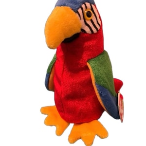 May include: A red, blue, green, and yellow plush parrot with a black and white striped eye patch. The parrot is a Ty Beanie Baby with a red heart tag.