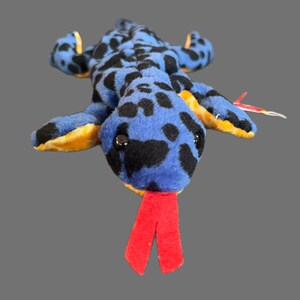 May include: Blue and black spotted plush toy lizard with a red tongue. The lizard has a yellow belly and is in a curled up position.