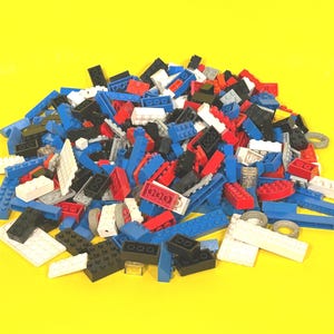 May include: A pile of colorful plastic building blocks in various shapes and sizes. The blocks are primarily red, blue, black, and white, with a few gray and green pieces. The background is a solid yellow.
