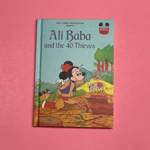 May include: A vintage children's book titled "Ali Baba and the 40 Thieves" featuring Mickey Mouse on the cover. The book is blue with a white border and features a cartoon illustration of Mickey Mouse in a red hat and blue shirt standing in a forest setting.