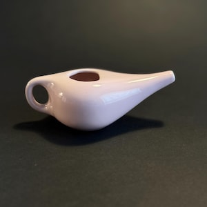 May include: A pale pink ceramic creamer with a handle and a spout. The creamer has a rounded body and a small opening at the top. The handle is a small loop. The spout is long and slender.