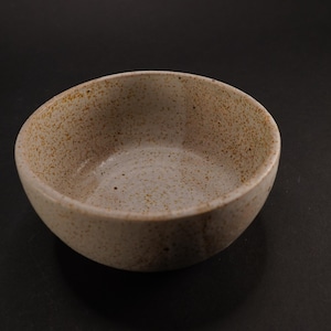 May include: A small, white ceramic bowl with a speckled, brown glaze. The bowl is round and has a slight lip.