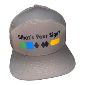 May include: A gray trucker hat with the text "What's Your Sign?" in black, along with colorful geometric shapes. The hat has a curved brim and a mesh back.