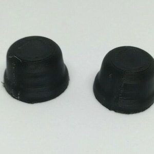 May include: Two black plastic caps with a ridged texture. The caps are round and have a slightly domed top.