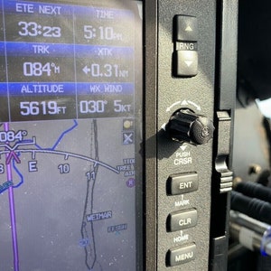 May include: A close-up of a small aircraft's instrument panel showing the altitude, heading, and other flight information. The panel has a black background with white text and numbers. The panel also has a small knob on the right side.