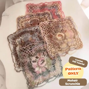 Può includere: Quattro scrunchies in mohair fatti a mano in vari colori, tra cui rosa, grigio e beige. Ogni scrunchie presenta un design all'uncinetto unico con accenti floreali. L'immagine include il testo "Pattern ONLY" e "Mohair Scrunchie".