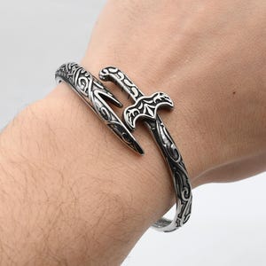 以下が含まれることがあります： 白いセラミックマグカップ、黒い持ち手、手書き風の「But First, Coffee」の文字。マグカップは白い面に置かれています。マグカップの高さは約10cmです。