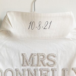 May include: White denim jacket with the text "MRS DONNELLY" in pearl embellishments and the date "10.8.21" written on the collar.