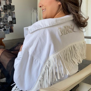 May include: A white denim jacket with fringe and a pearl embellished "MRS" patch on the back.