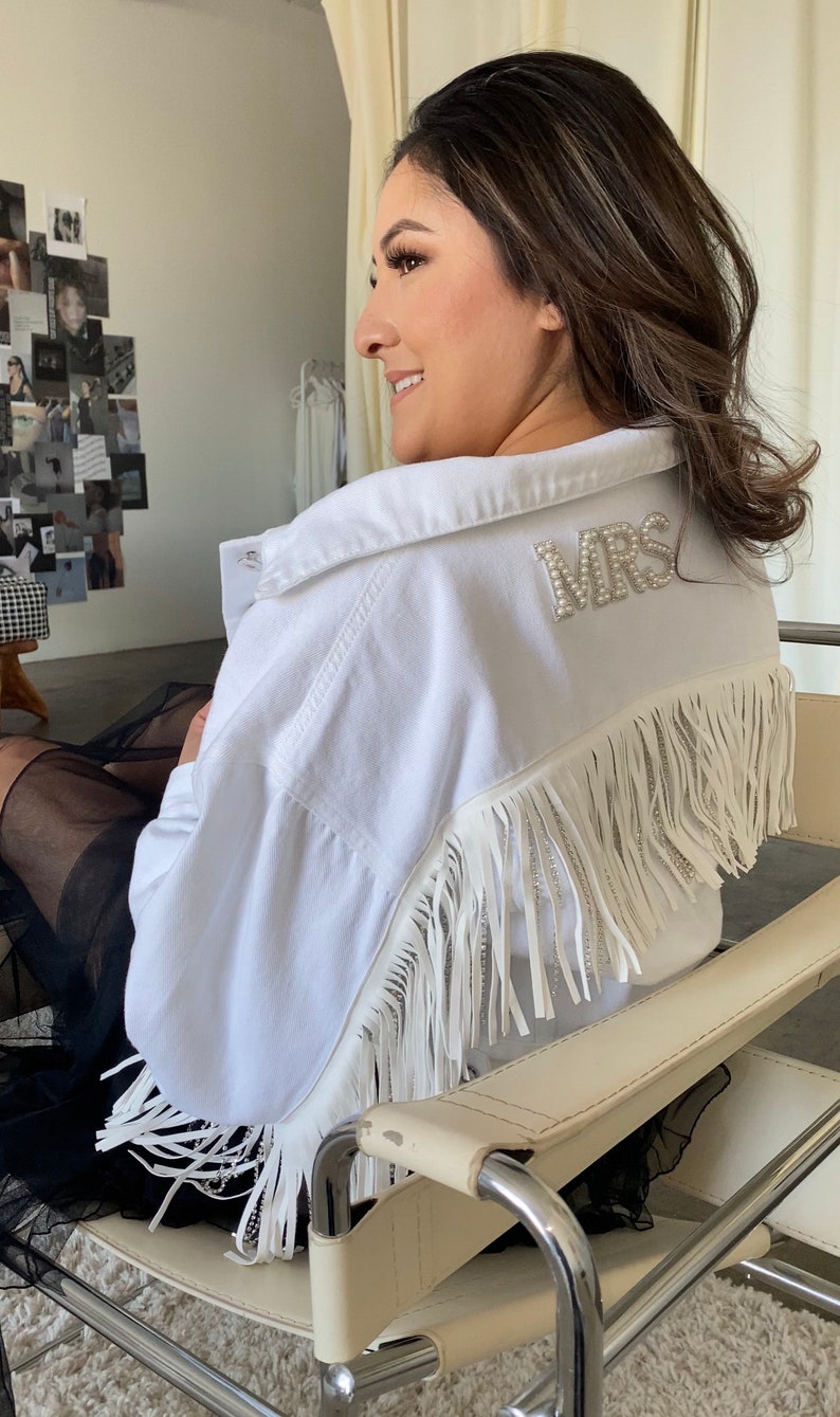 May include: A white denim jacket with fringe and a pearl embellished "MRS" patch on the back.
